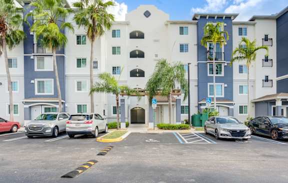 A parking lot in front of a multi-story building with cars parked.