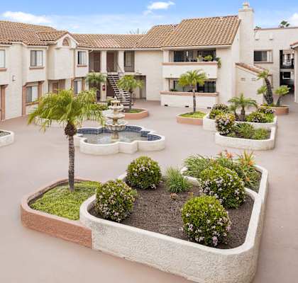 A courtyard with a fountain and plants in the middle of apartment buildings.