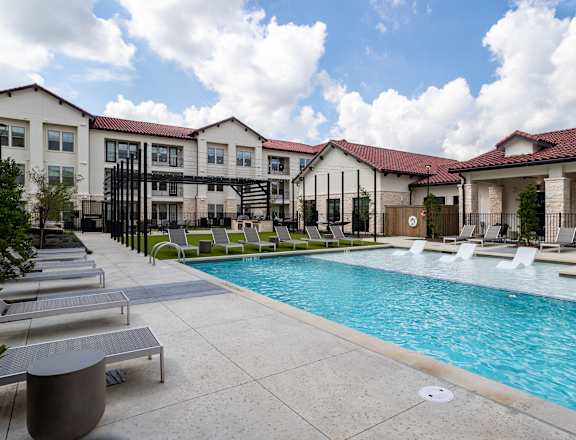 A pool area with sun loungers and a building in the background.