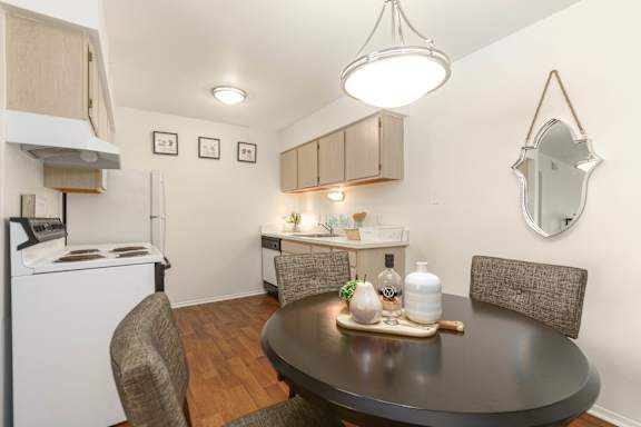 A kitchen with a table and chairs in the foreground and a refrigerator and cabinets in the background.