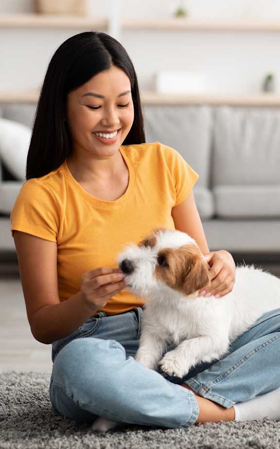 A woman is sitting on the floor with a small white and brown dog.