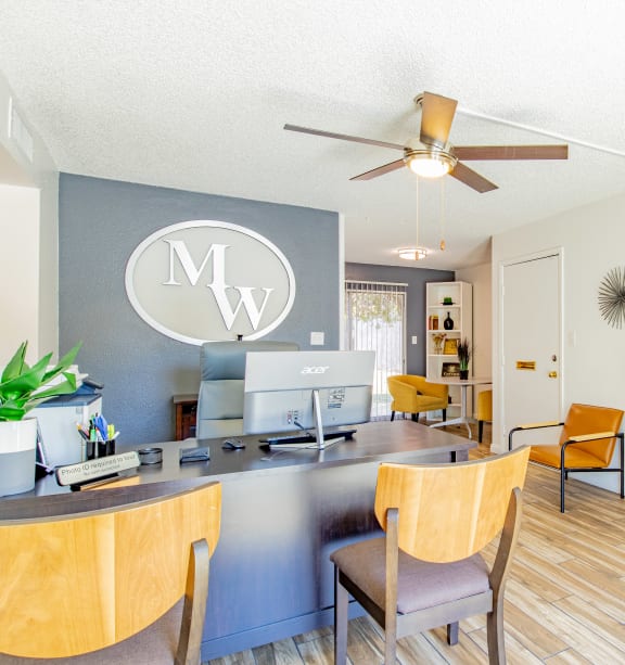 a living room with a desk and chairs and a ceiling fan