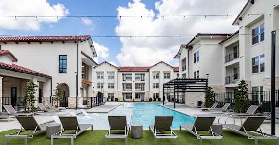 A pool surrounded by lawn chairs and buildings in the background.