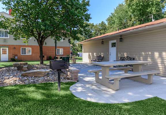 a patio with a picnic table and grill in front of a house