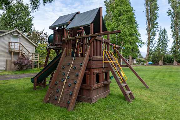 A wooden playhouse with a green slide and yellow stairs.