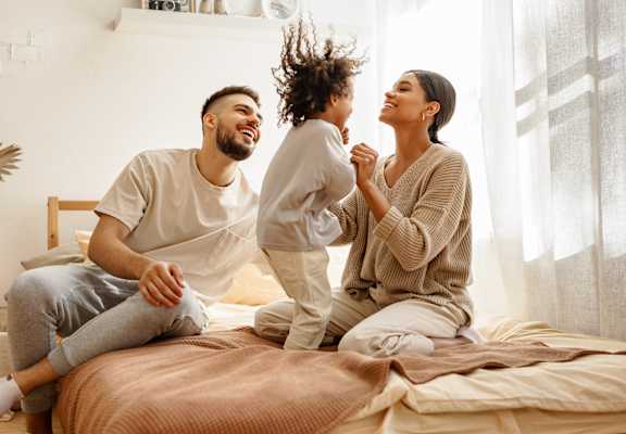 A man and woman are sitting on a bed with a child jumping on them.