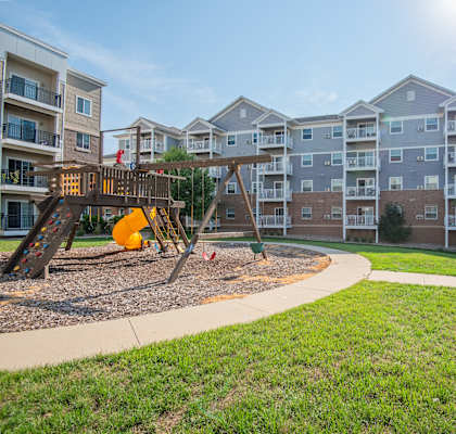 a playground with a swing set in front of an apartment building