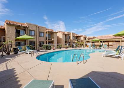 A swimming pool surrounded by lounge chairs and umbrellas in a sunny day.