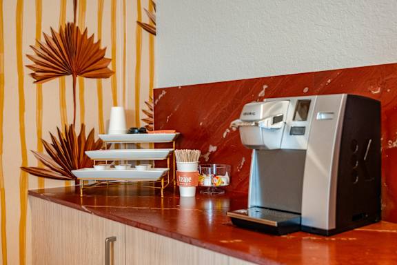 A coffee machine is on a counter with a stack of white plates and cups.