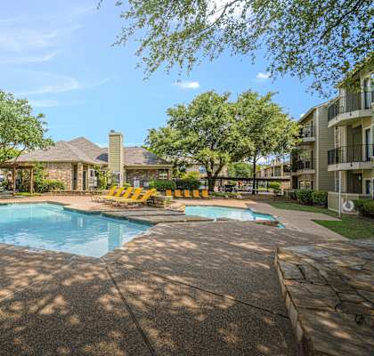 A large swimming pool surrounded by a stone wall and yellow chairs.