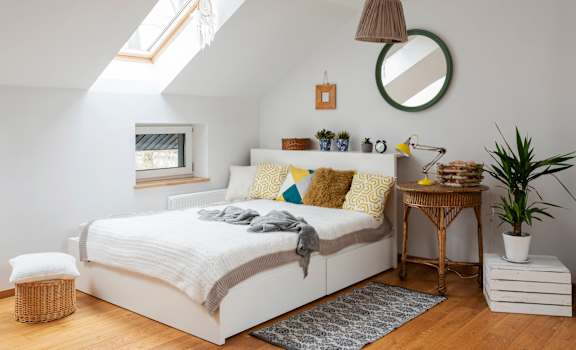 A bedroom with a bed, a mirror, a lamp, and a plant.