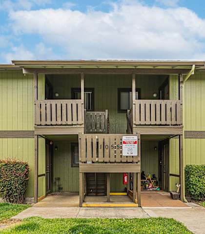 A green two-story apartment building with a balcony on the second floor.