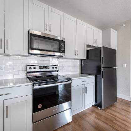 a kitchen with stainless steel appliances and white cabinets at The Junction at Rogers, Rogers
