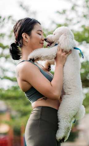 A woman holding a white dog in a park.