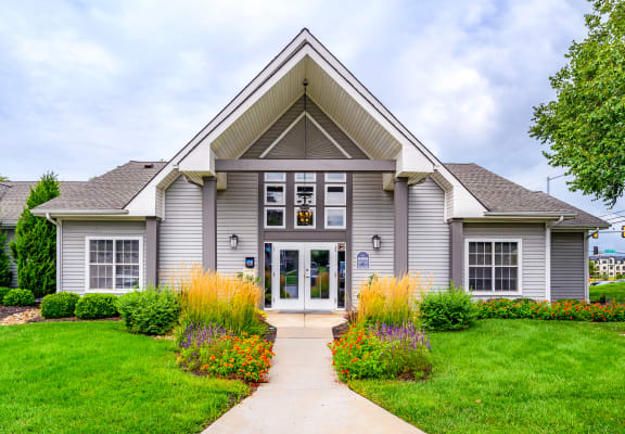 the front of a gray house with a green lawn and colorful flowers
