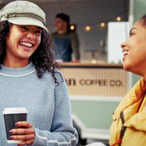 A woman in a grey sweater and cap is holding a coffee cup.