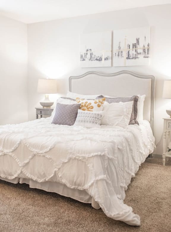 a white bedroom with a bed and pillows and a painting on the wall