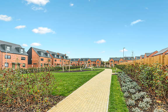 A long pathway leads through a grassy area between two rows of houses.