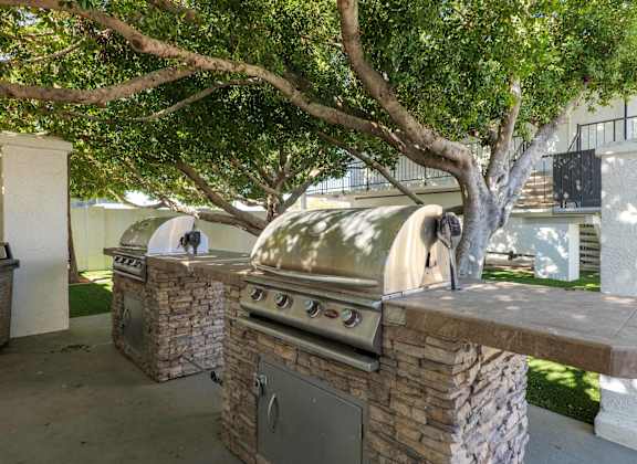 A large outdoor grill is built into a stone wall under a tree.
