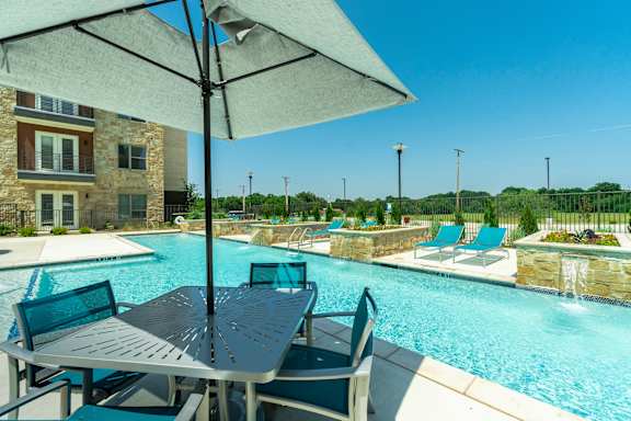 A poolside table with chairs and an umbrella overlooking a pool.