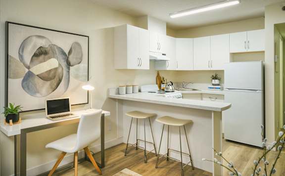 A modern kitchen with a white chair and a laptop on the desk.