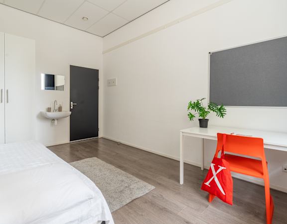 A bedroom with a white bed, a red chair, and a small table with a plant on it.