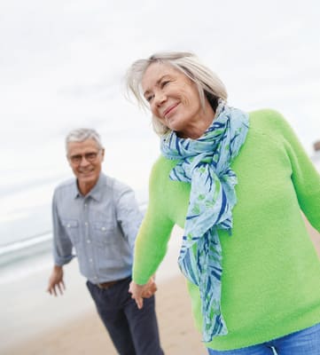 An older couple holding hands and walking on the beach