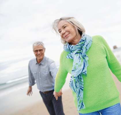 An older couple holding hands and walking on the beach