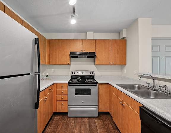 A kitchen with a stainless steel refrigerator, a stove, and wooden cabinets.