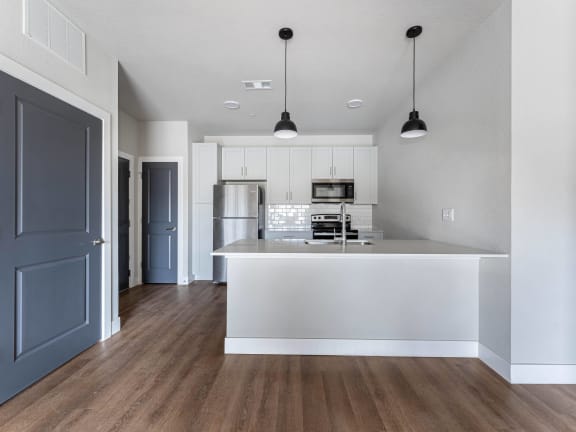 an open kitchen and living room with a white island and a blue door at The Junction at Rogers, Rogers