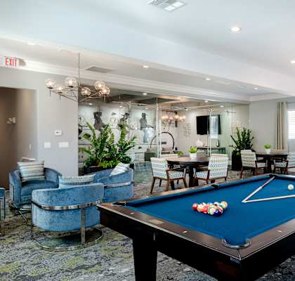 A pool table is in the middle of a room with a blue chair and a mirror.