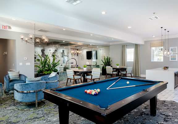 A pool table is in the middle of a room with a blue chair and a mirror.