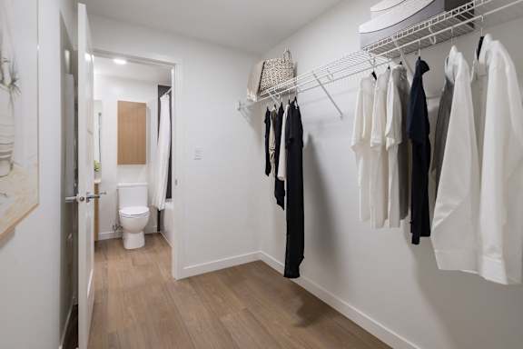 A hallway with a toilet and clothes hanging up.