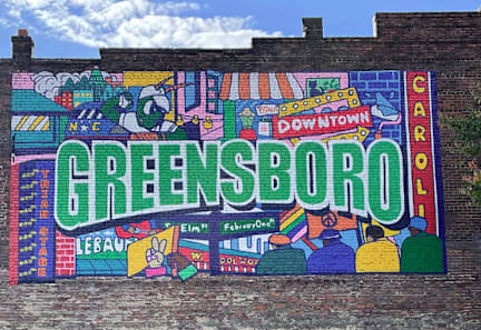 A colorful mural on a brick wall with the word "GREENSBORO" prominently displayed.