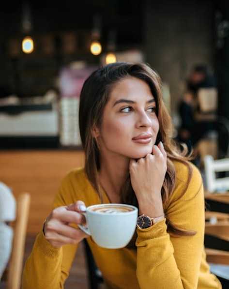 A woman in a yellow sweater is holding a cup of coffee.