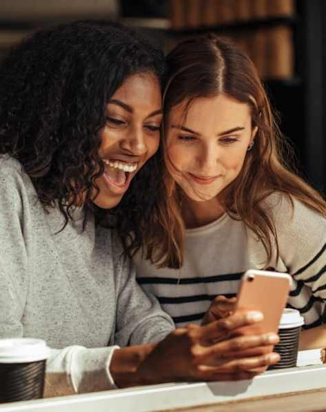 Two women are laughing while looking at a smartphone.
