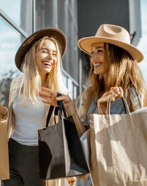 Two women wearing hats and holding shopping bags.