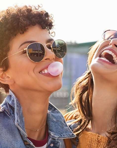 Two people wearing sunglasses and a denim jacket are laughing.