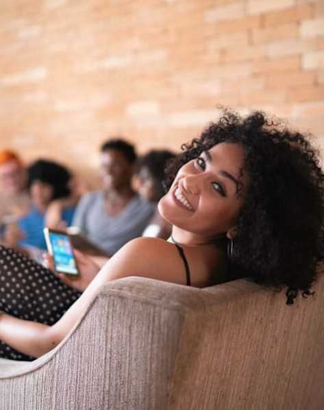 A woman with curly hair is sitting on a couch looking at her phone.
