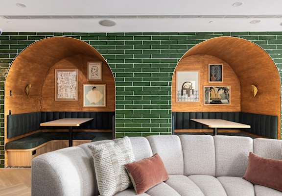 A grey couch with two pillows sits in front of a green tiled wall with two wooden arches above it.
