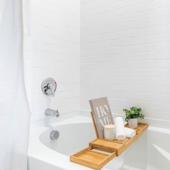 a white bathtub with a wooden tray with candles and a sign in the tub