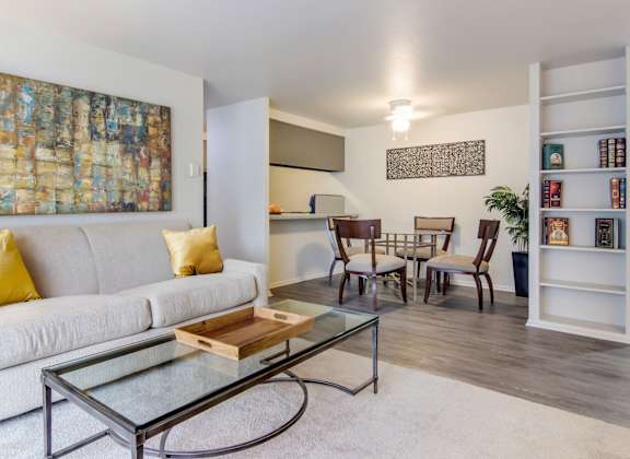 A living room with a white couch, a glass coffee table, and a painting on the wall.