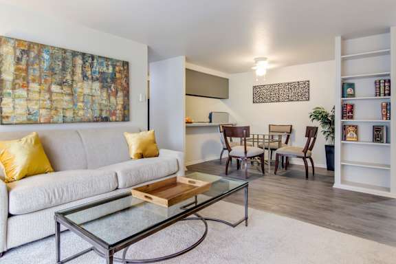 A living room with a white couch, a glass coffee table, and a painting on the wall.