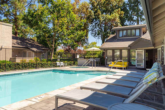 A pool with sun loungers and a house in the background.
