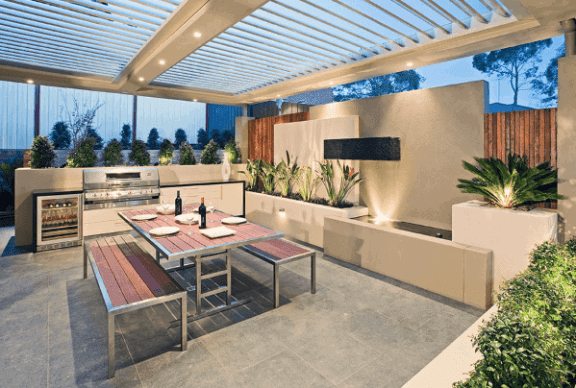 an outdoor kitchen and dining area under a glass roof