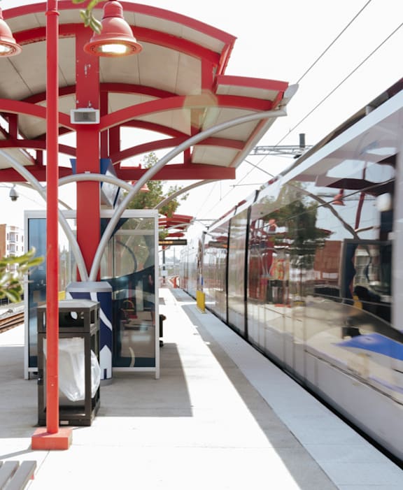 A train station with a train on the tracks and a red and white canopy.