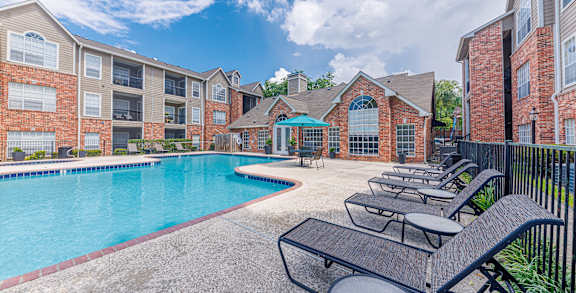 A pool surrounded by lounge chairs and a brick building.