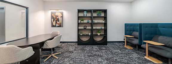 A modern office space with a grey carpet, a round table, and a clock on the wall.