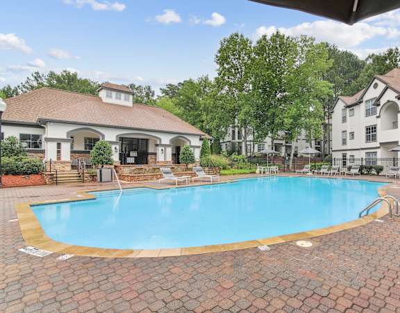 A large outdoor swimming pool surrounded by a brick patio and lounge chairs.