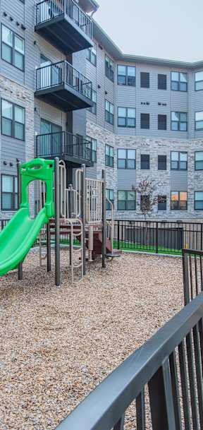 A green slide is in the playground of apartment buildings.